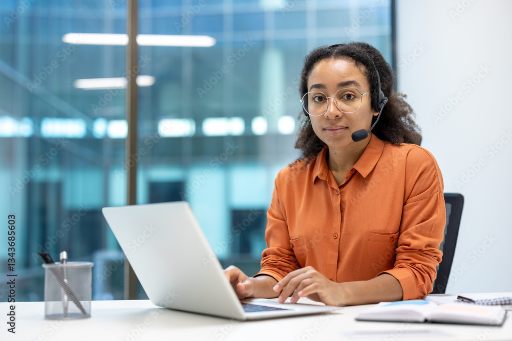 Portrait of serious focused woman with headset, customer support worker inside office at workplace, using laptop for video call. Looking thoughtfully at camera Portrait of serious focused woman with headset, customer support worker inside office at workplace, using laptop for video call. Looking thoughtfully at camera