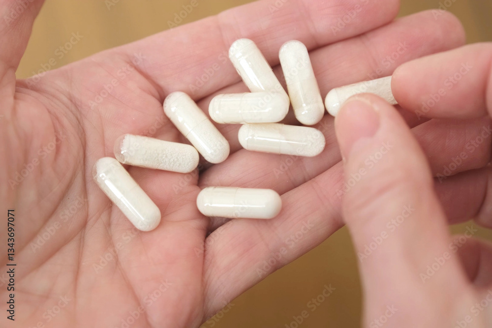 Hand is holding multiple white capsules, perhaps supplements or medication, on a neutral background. Fingers gently grasp the pills, showcasing them in an open palm. Hand is holding multiple white capsules, perhaps supplements or medication, on a neutral background. Fingers gently grasp the pills, showcasing them in an open palm.