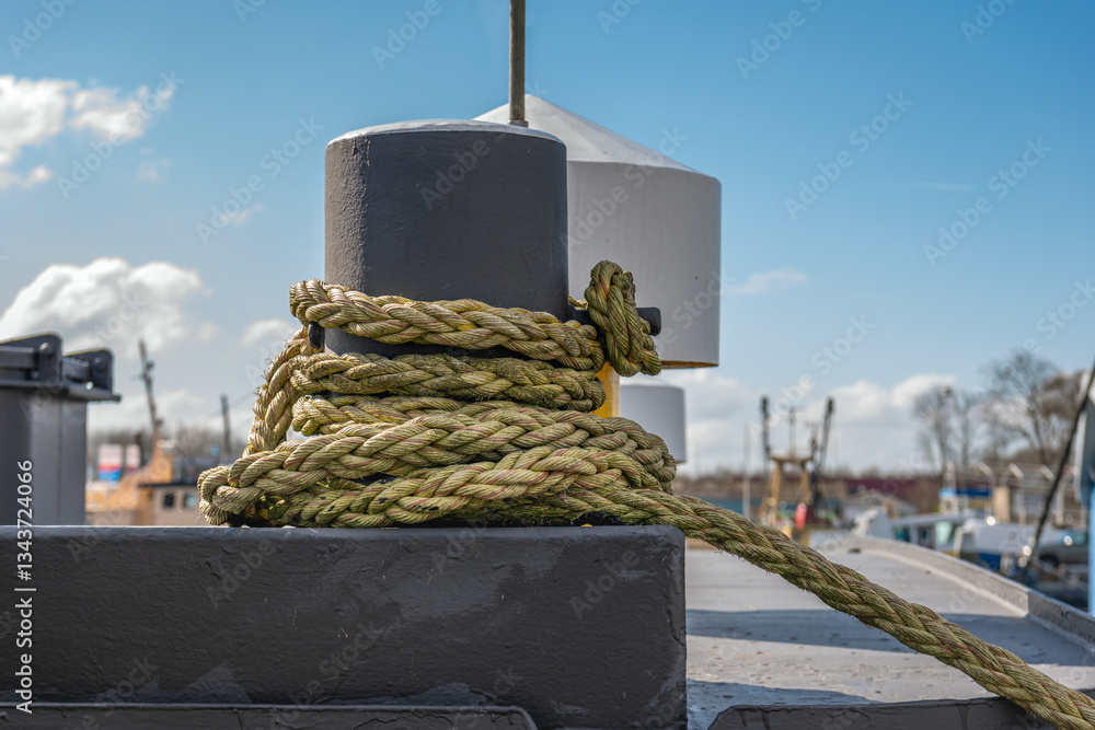 Closeup of a thick rope around a bollard on the deck of a cargo ship moored in the harbor.