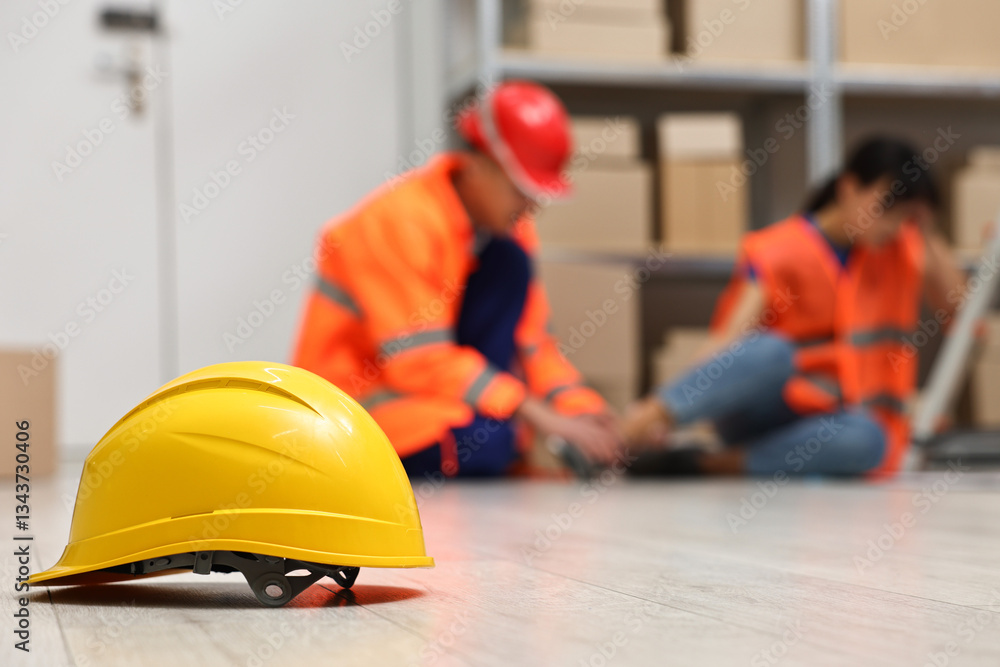 Accident at work. Hardhat on floor and man helping his injured colleague in warehouse, selective focus Accident at work. Hardhat on floor and man helping his injured colleague in warehouse, selective focus