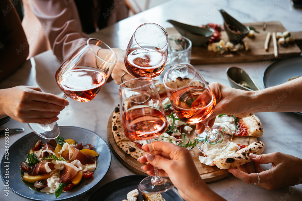 Friends enjoy a dinner party with pizza and rose wine in a bar or a restaurant.