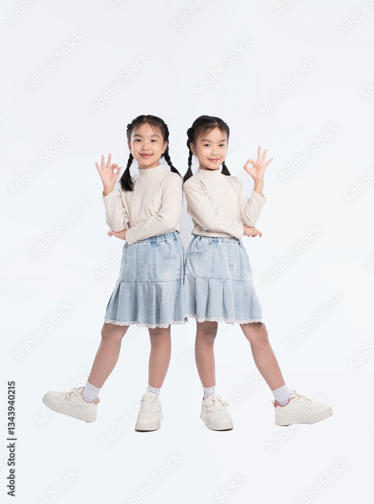 Two young girls with braided hair in matching outfits posing in front of a white background. Okay sign gesture. Two young girls with braided hair in matching outfits posing in front of a white background. Okay sign gesture.