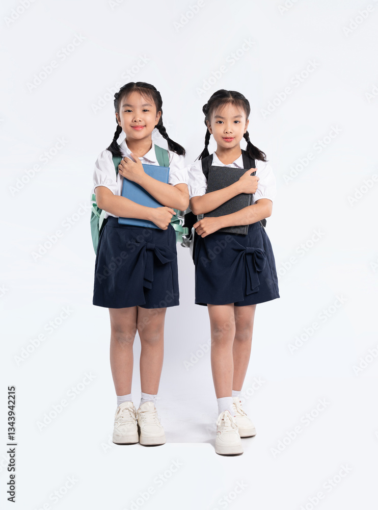 Two young students pose with their books and backpacks, ready for school, in matching uniforms. Two young students pose with their books and backpacks, ready for school, in matching uniforms.