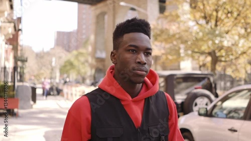 Young black male fashion model walking through the streets of New York City with Skateboard under his arm.