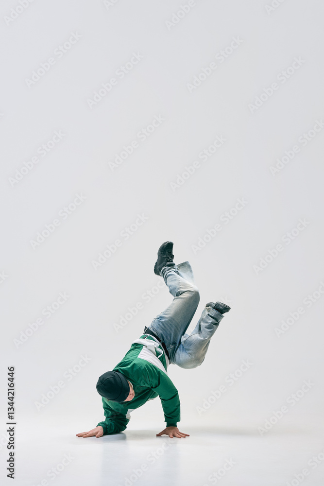 Breakdancer twisting mid-air while balancing on hands, showcasing flexibility and agility against white studio background. Concept of sport, art, dance, perseverance, modern urban culture. Breakdancer twisting mid-air while balancing on hands, showcasing flexibility and agility against white studio background. Concept of sport, art, dance, perseverance, modern urban culture.