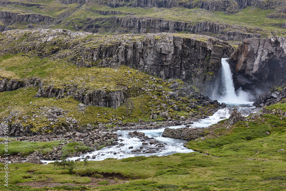 Waterfall and basalt rocks covered by moss. Seydisfjordur. Iceland