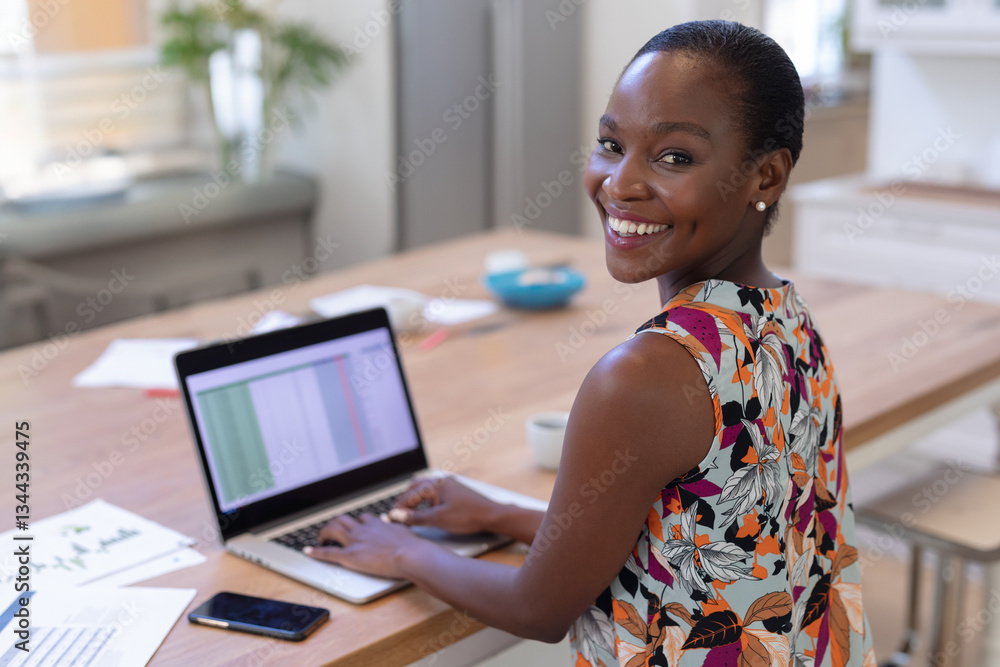 Smiling woman working on laptop at home, multitasking with smartphone nearby, copy space