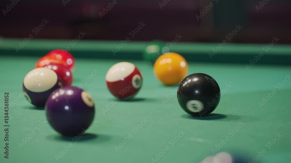 Close-up of hand rolling black billiard ball on green pool table, surrounded by vibrant colorful balls. Focus on motion, precision, and dynamics of gameplay as ball moves across smooth felt surface