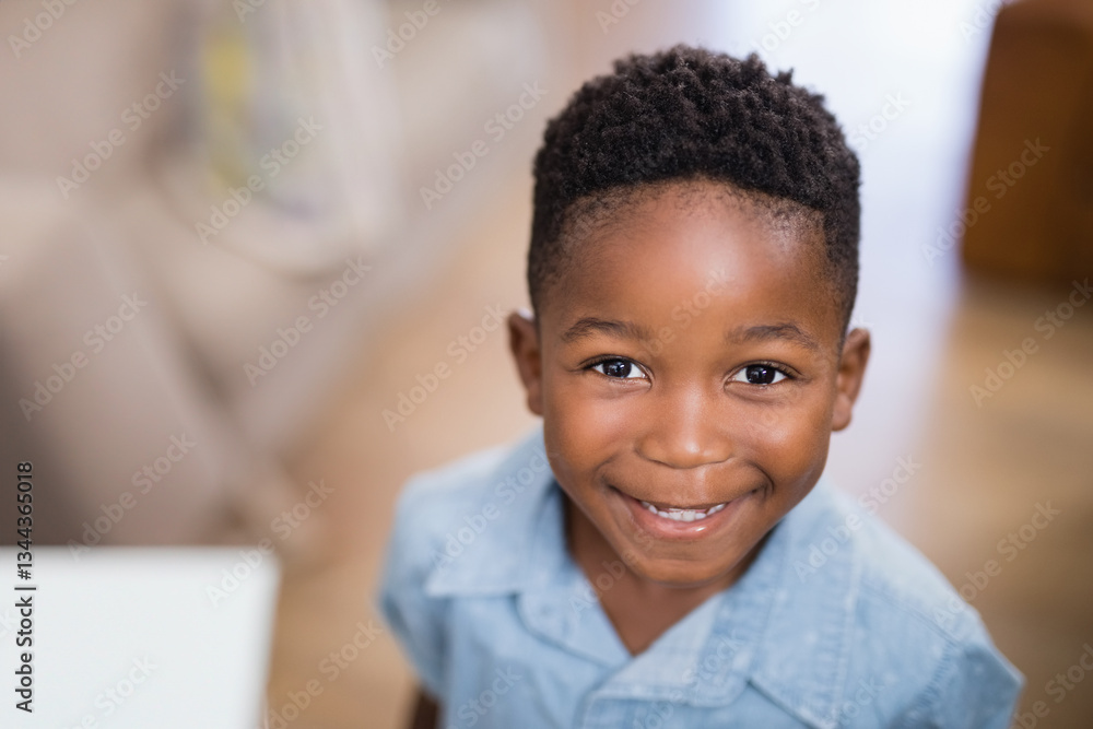 Naklejka premium Smiling young boy at home, wearing blue shirt, looking at camera happily