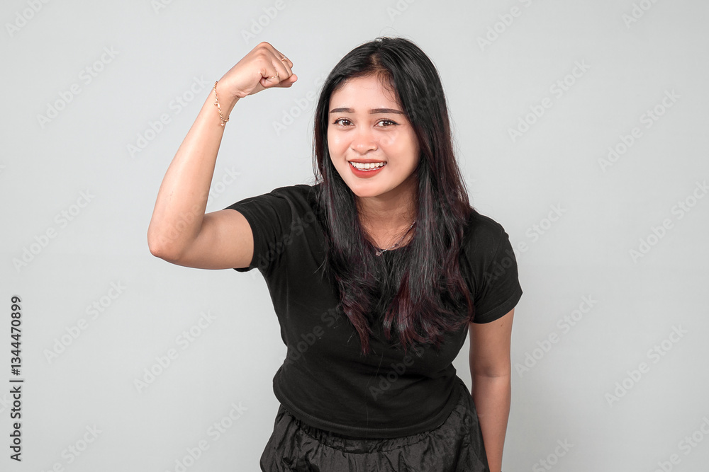 A cheerful Indonesian woman in a black outfit raises her fist in a victory pose, smiling with confidence. She looks strong, happy, and motivated, expressing excitement and energy. A cheerful Indonesian woman in a black outfit raises her fist in a victory pose, smiling with confidence. She looks strong, happy, and motivated, expressing excitement and energy.