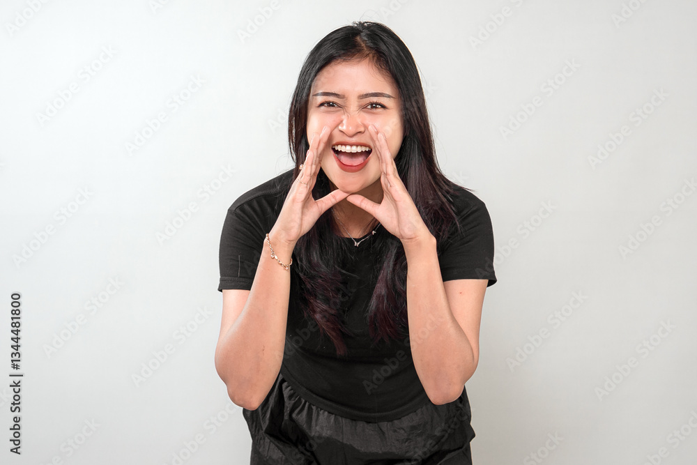 An Indonesian woman in black clothes shouts with excitement, cupping her hands around her mouth. Her joyful expression and energetic pose convey enthusiasm and happiness. An Indonesian woman in black clothes shouts with excitement, cupping her hands around her mouth. Her joyful expression and energetic pose convey enthusiasm and happiness.