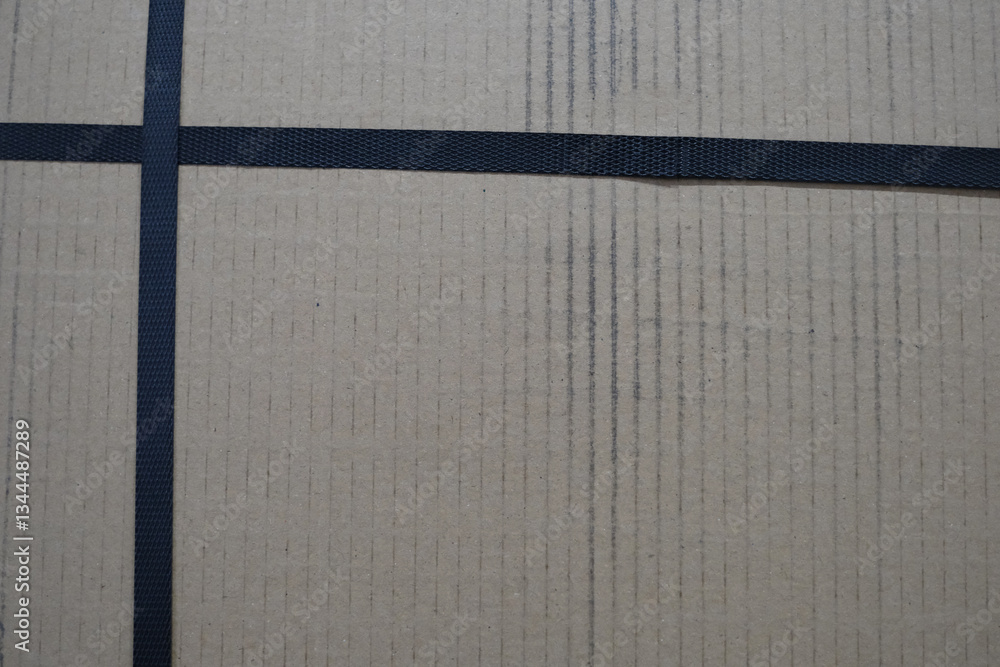 Fototapeta premium A cardboard box with a black tape running across it. The box is brown and has a cross pattern on it