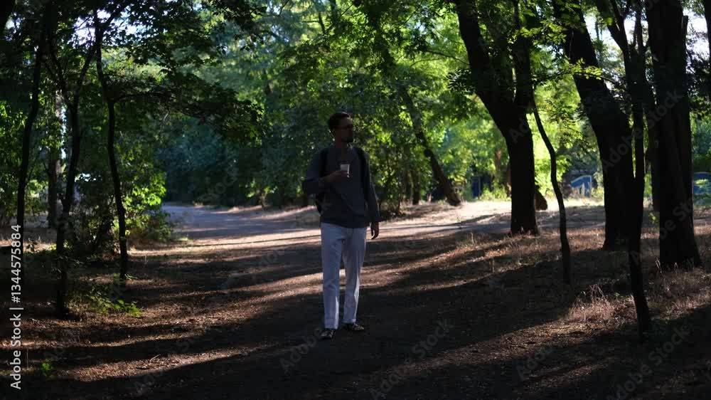 Young handsome man walking in the park on a sunny summer morning with coffee Young handsome man walking in the park on a sunny summer morning with coffee