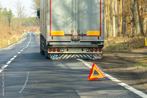 truck breakdown.broken truck with semi-trailer on national road. warning triangle displayed on the road. flat tire on semi-trailer.