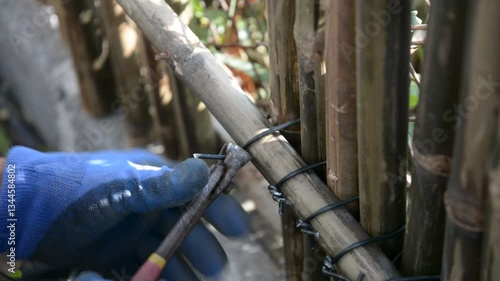 Worker install bamboo wall panels tied together with aluminum wire to cover a chain link fence.