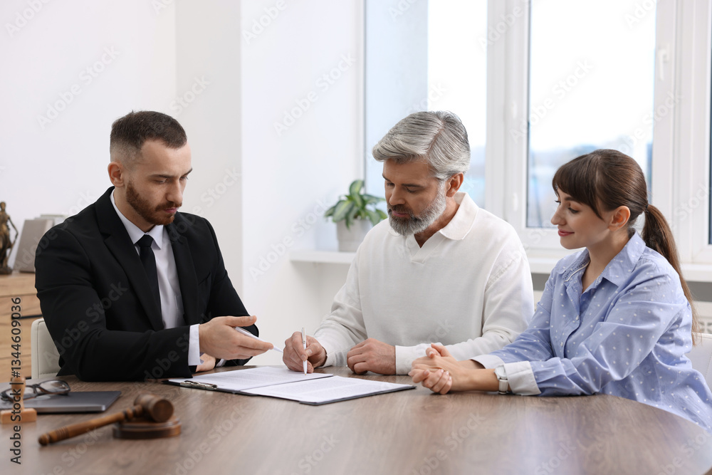 Clients signing notarial paperwork during meeting with lawyer at wooden desk indoors Clients signing notarial paperwork during meeting with lawyer at wooden desk indoors
