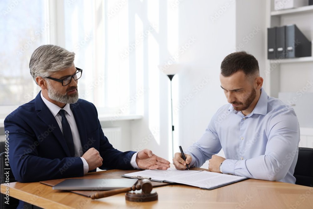 Client signing notarial paperwork during meeting with lawyer at wooden desk indoors Client signing notarial paperwork during meeting with lawyer at wooden desk indoors