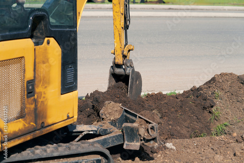 The miniature excavator digs a trench in tight spaces on a narrow road divider. It is additionally equipped with a mounted moldboard.