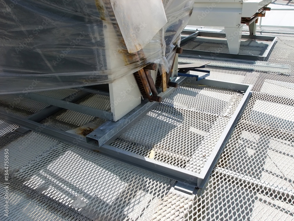 Fototapeta premium A rooftop HVAC unit partially covered in plastic wrap sits on a diamond-patterned metal floor.