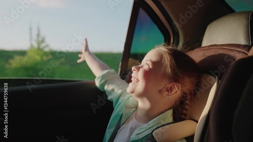 Happy child enjoying car ride, girl smiling backseat, kid feeling wind through the window, road trip with family, joyful childhood moment, excited young traveler, summer adventure road, cheerful