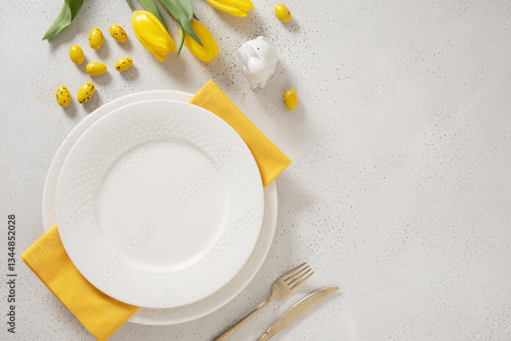 Easter table setting with spring, yellow tulips, white plates, bunny, eggs on white background. Festive place setting. Holidays background. Copy space. View from above.