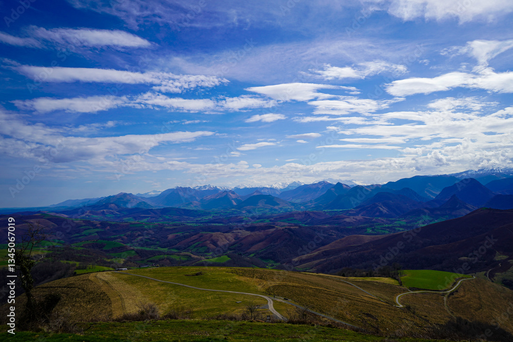 Naklejka premium Winding Roads Along Grassy Hills With Snowy Mountains In The Distance With Cloudy Blue Sky