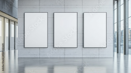Three large blank posters with black frames mounted on a concrete office wall, surrounded by glass windows and reflecting city buildings.