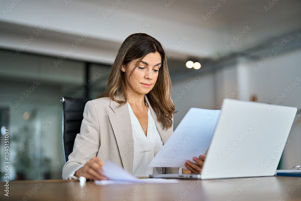 Busy serious mid aged business woman working in office with laptop reading document. Mature professional female manager lawyer attorney holding paper finance report sitting at desk in office. Busy serious mid aged business woman working in office with laptop reading document. Mature professional female manager lawyer attorney holding paper finance report sitting at desk in office.