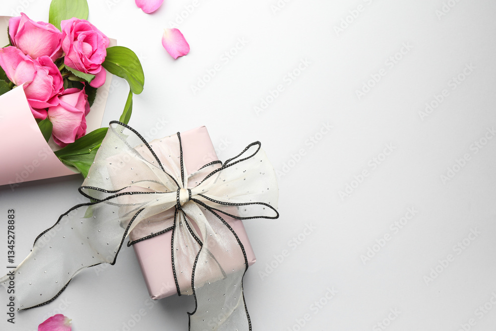 Fototapeta premium Gift box with beautiful bow and pink roses on light background, flat lay. Space for text