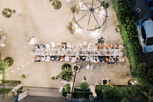 USA, Miami - March 29, 2024: Guests sit at a long festive table in the courtyard of a house with lighting. Drone