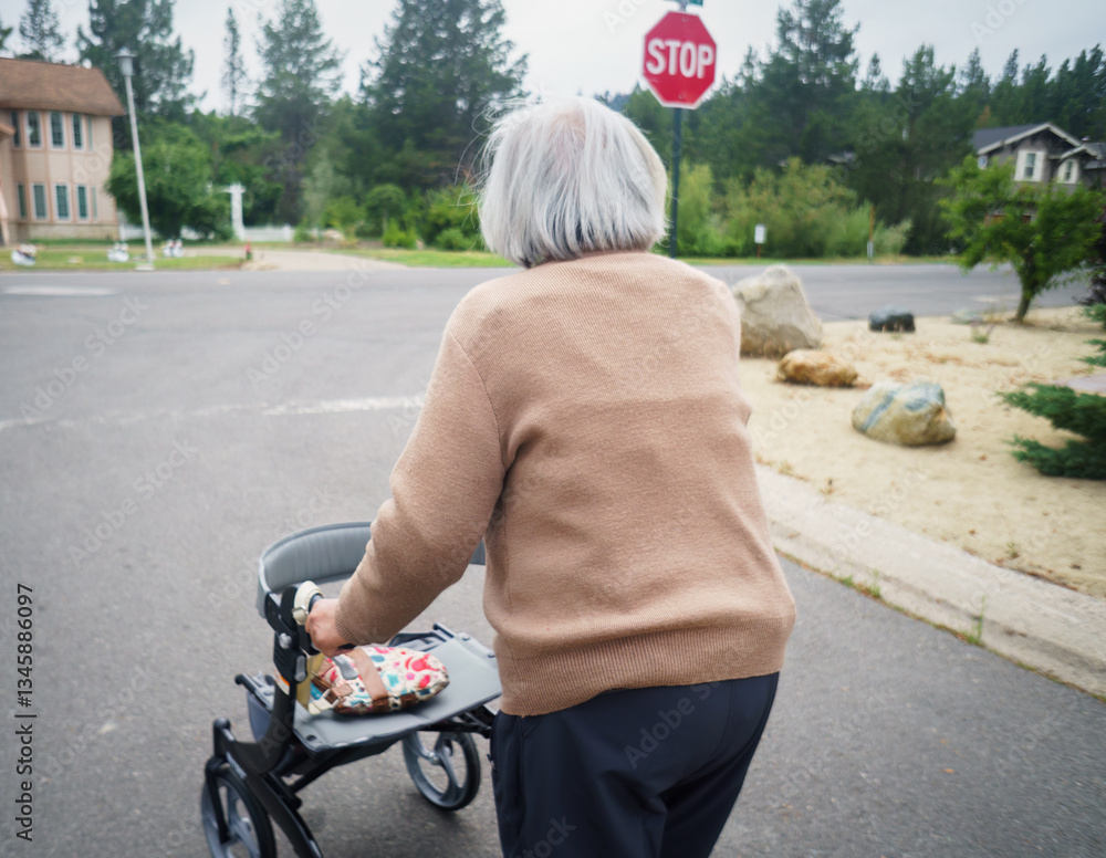A senior woman walking with a mobility walker. STOP road sign at the corner of the intersection. California.