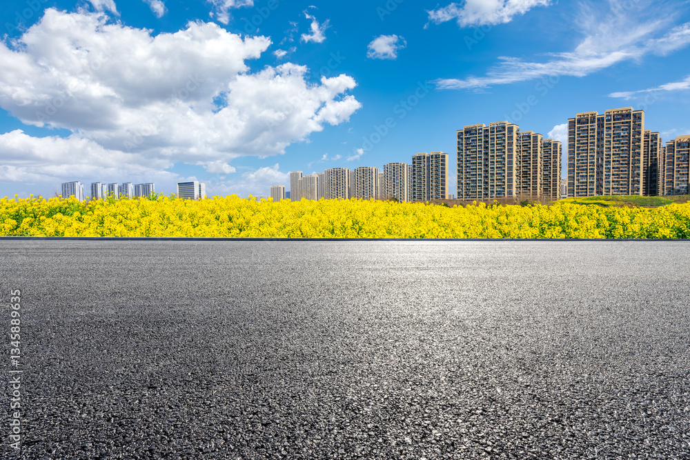 Asphalt road and yellow canola flowers with buildings in the city