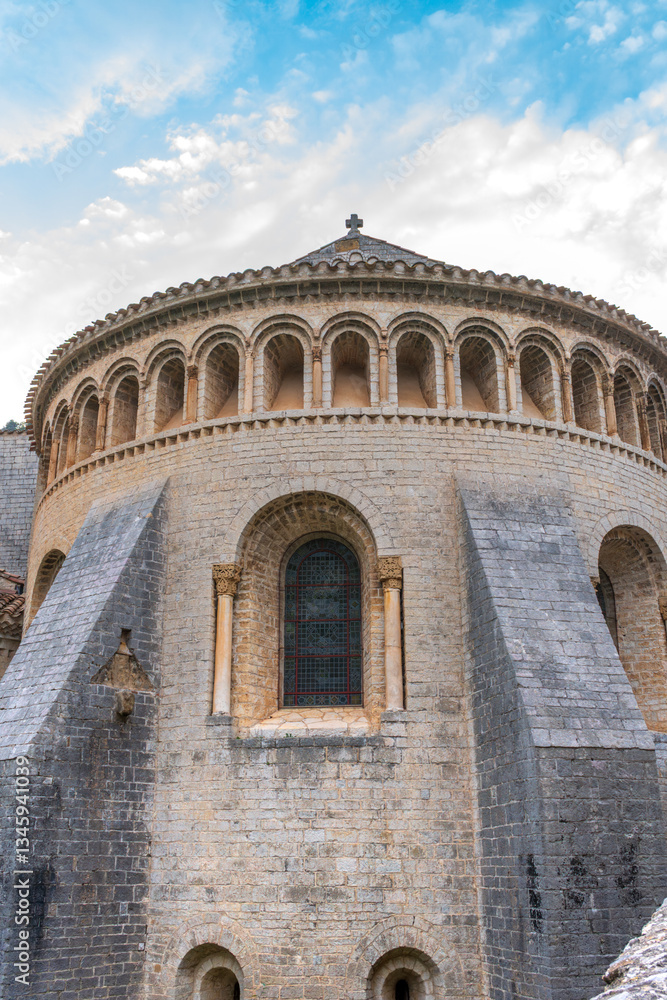Fototapeta premium Ancient Romanesque church with arched windows and stone walls, featuring a stained-glass window, buttresses, and a blue sky