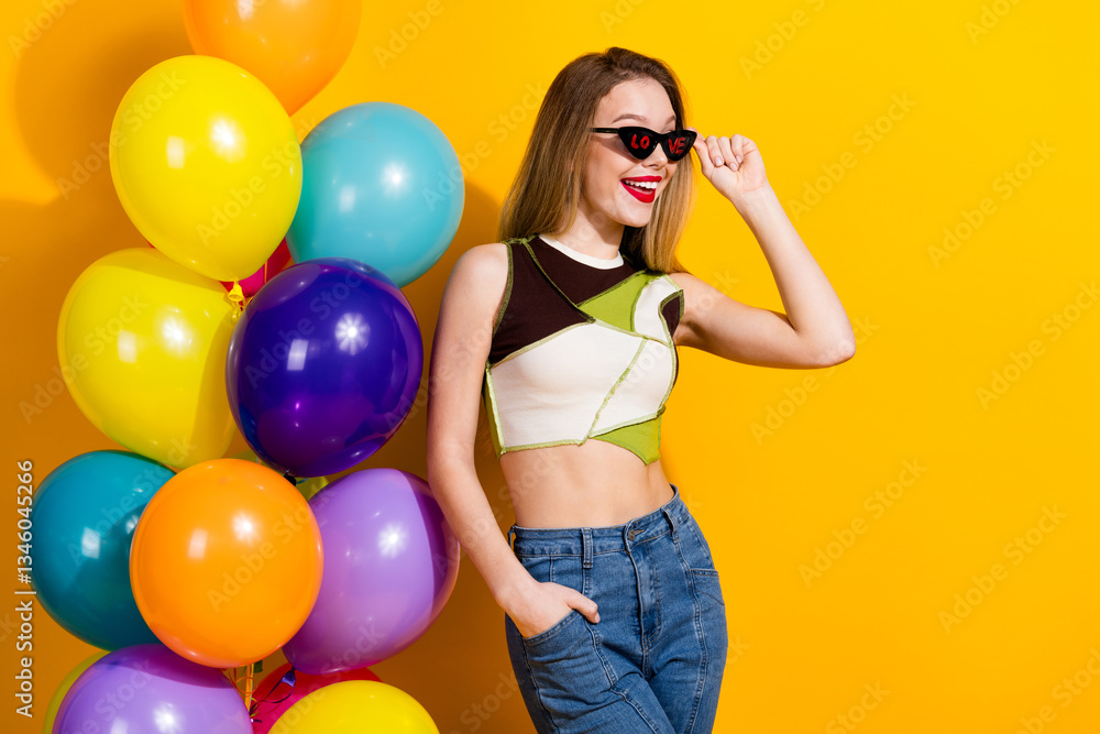 Stylish young woman smiling with sunglasses and balloons against yellow background, expressing happiness and summer vibes Stylish young woman smiling with sunglasses and balloons against yellow background, expressing happiness and summer vibes