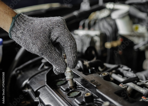 Male hand replacing spark plug in gasoline engine with engine compartment background. Car repair and maintenance concept.
