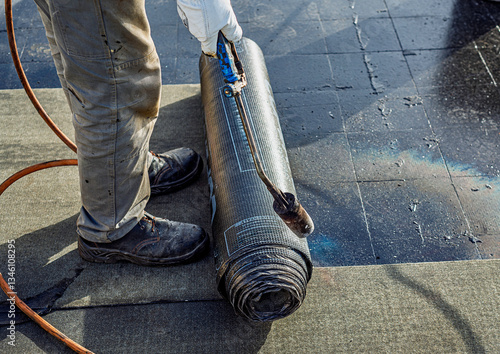 Roof waterproofing with bituminous membrane being installed. Close-up on the worker's feet and the membrane roll, showcasing the application process. Fata Morgana effect