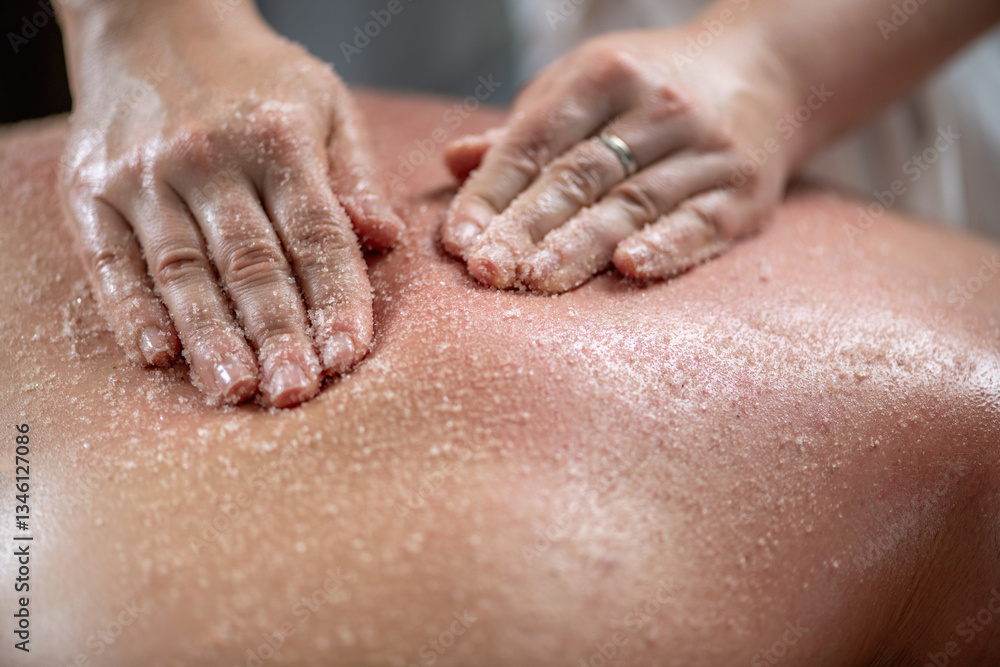 Fototapeta premium Scrubbing back massage with salts exfoliates the skin, removes dead skin cells, unclogs pores, and promotes smoother, healthier skin, offering relaxation and revitalization in a spa setting