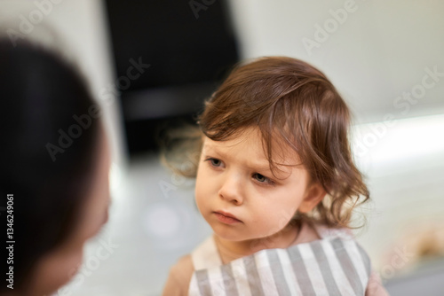 Φωτογραφία offended little child girl in striped apron talks to mom in kitchen, mom forbade