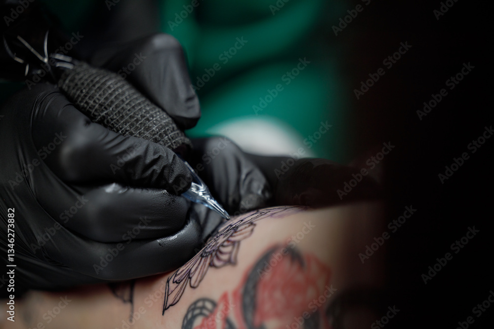 Fototapeta premium Close up tattoo master professional tattoo artist in black gloves making a rose tattoo on a man's forearm. He is holding a tattoo machine.