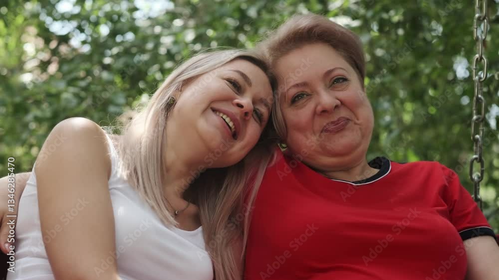 An adult mother with a young daughter swinging on a swing in the garden next to her house. Hugging, talking and laughing. An adult mother with a young daughter swinging on a swing in the garden next to her house. Hugging, talking and laughing.