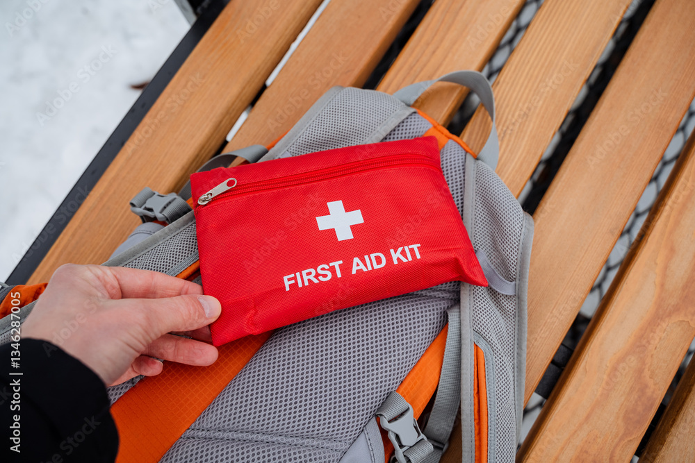 Naklejka premium A person is currently holding a first aid kit over the top of a backpack, which is resting on the ground. This shows the importance of being prepared for emergencies while traveling