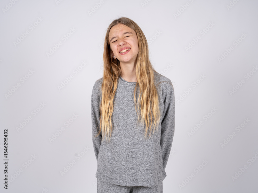 Obraz premium Positive beautiful caucasian girl wearing grey track-suit with overjoyed expression closes eyes and laughs shows white perfect teeth