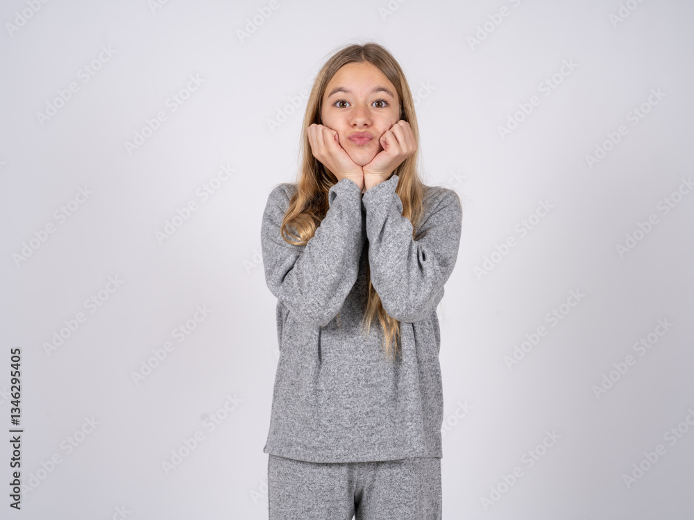 beautiful caucasian girl wearing grey track-suit with surprised expression keeps hands under chin keeps lips folded makes funny grimace beautiful caucasian girl wearing grey track-suit with surprised expression keeps hands under chin keeps lips folded makes funny grimace