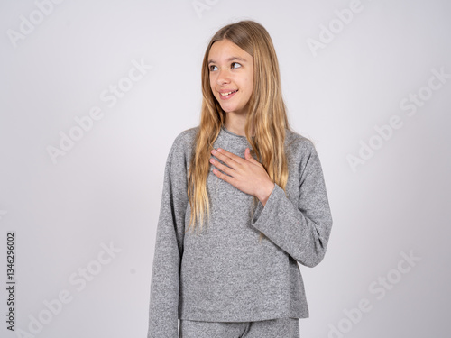 Joyful beautiful caucasian girl wearing grey track-suit  expresses positive emotions recalls something funny keeps hand on chest and giggles happily. photo