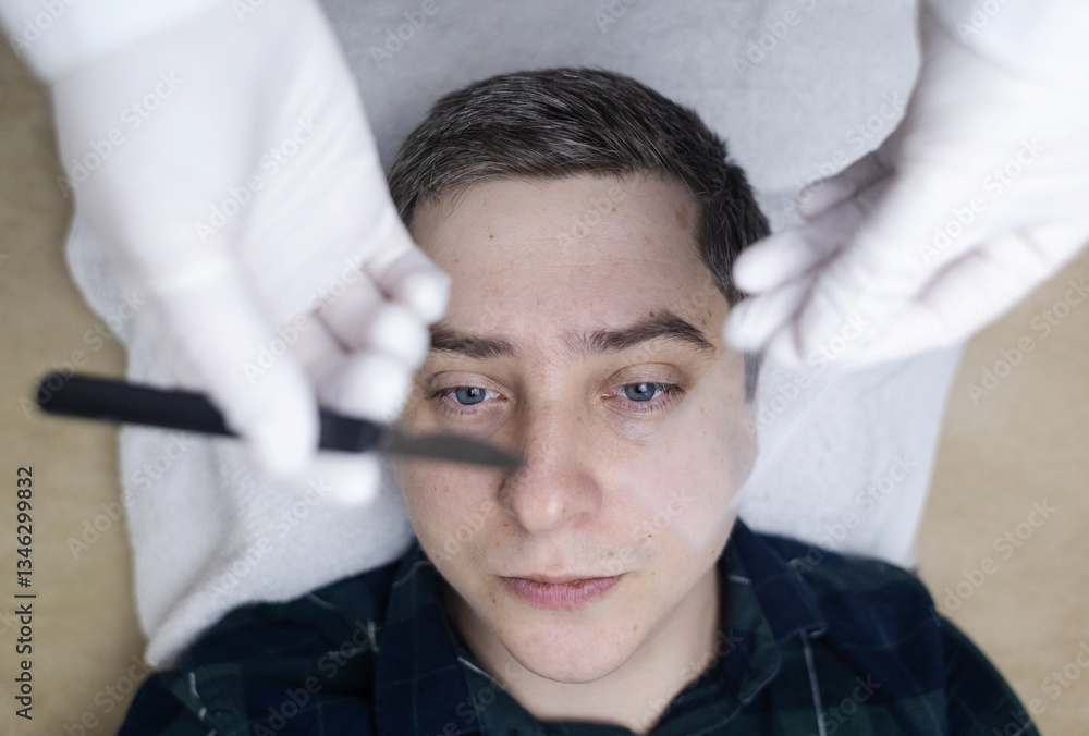 Fototapeta premium A dermatologist takes a skin scraping test for demodicosis and dermatitis, fungal infection. Close-up of a male patient's face at a doctor's appointment