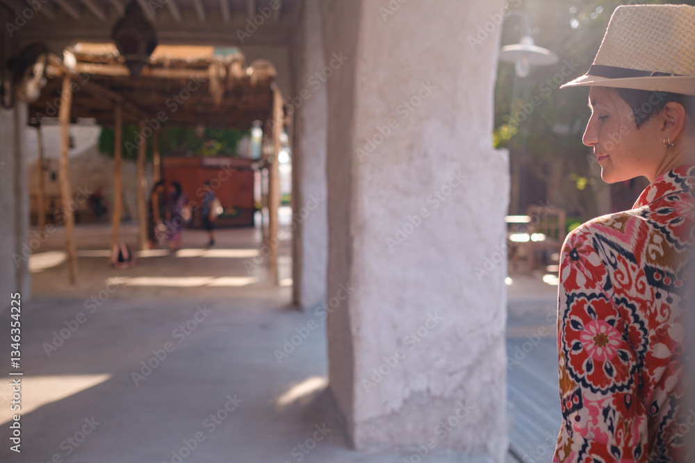 Obraz premium Young woman in an ethnic dress and hat exploring Al Seef Park in Dubai. Surrounded by traditional Emirati architecture and modern vibes, she enjoys the charm of Dubai Creek's cultural heritage.