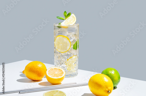 Lemonade with lemon, mint and ice in a glass on a white gray background with shadow and fruits.