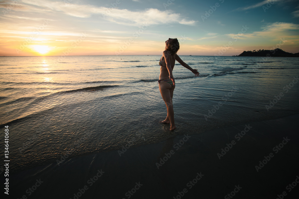 A woman in a swimsuit greets the sunrise on the beach, embodying relaxation and tranquility in a serene morning setting.