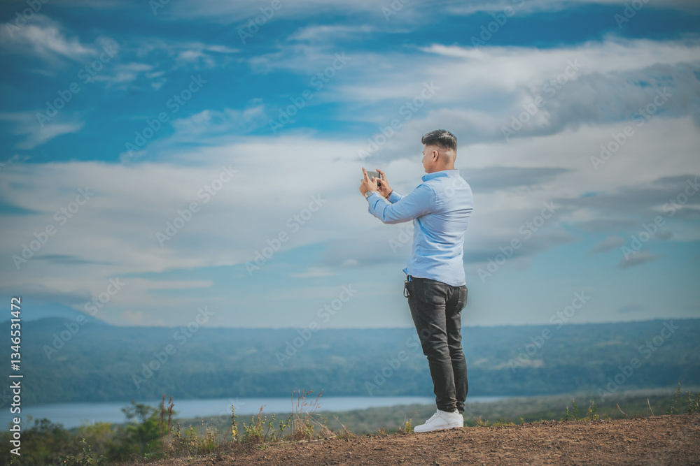 Young man taking photos with cell phone at a natural viewpoint. Tourist taking photos with phone at a volcanic viewpoint, Masaya, Nicaragua Young man taking photos with cell phone at a natural viewpoint. Tourist taking photos with phone at a volcanic viewpoint, Masaya, Nicaragua