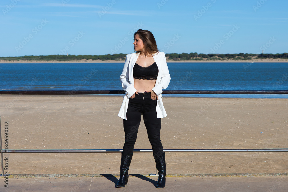 Young and beautiful blonde woman is leaning on the railing of the promenade at the mouth of the river, the woman looks to the side. In the background the blue sea. Young and beautiful blonde woman is leaning on the railing of the promenade at the mouth of the river, the woman looks to the side. In the background the blue sea.